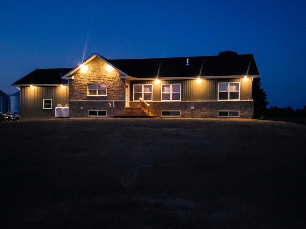 Stone and siding home glowing with exterior lighting installed at dusk