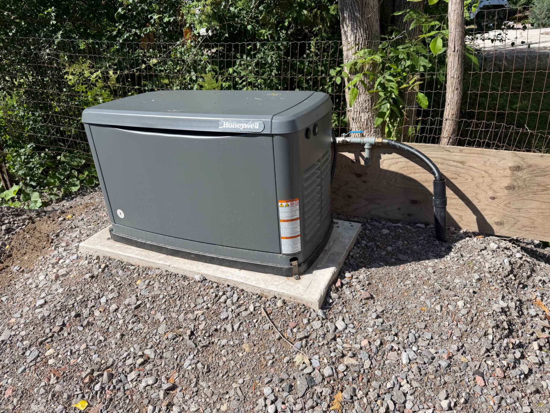 Honeywell standby generator installed on a gravel pad beside a home